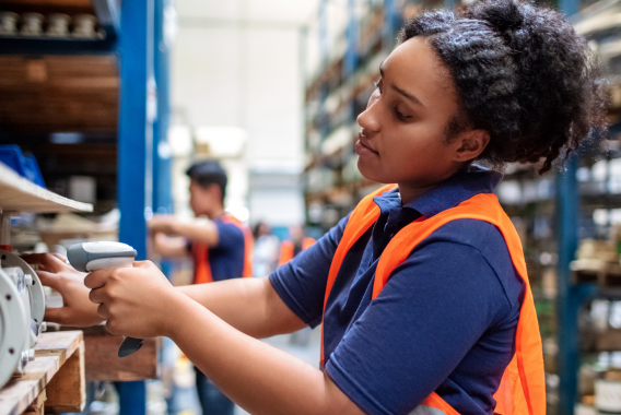 Frau, die ein Produkt mit einem Barcode-Scanner in einem Lager scannt