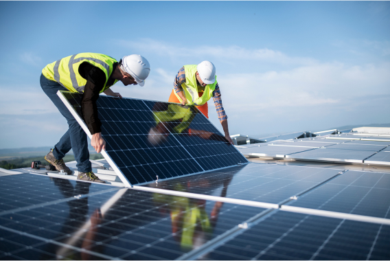 Zwei Arbeiter mit Schutzhelmen, die Solarmodul auf dem Dach halten