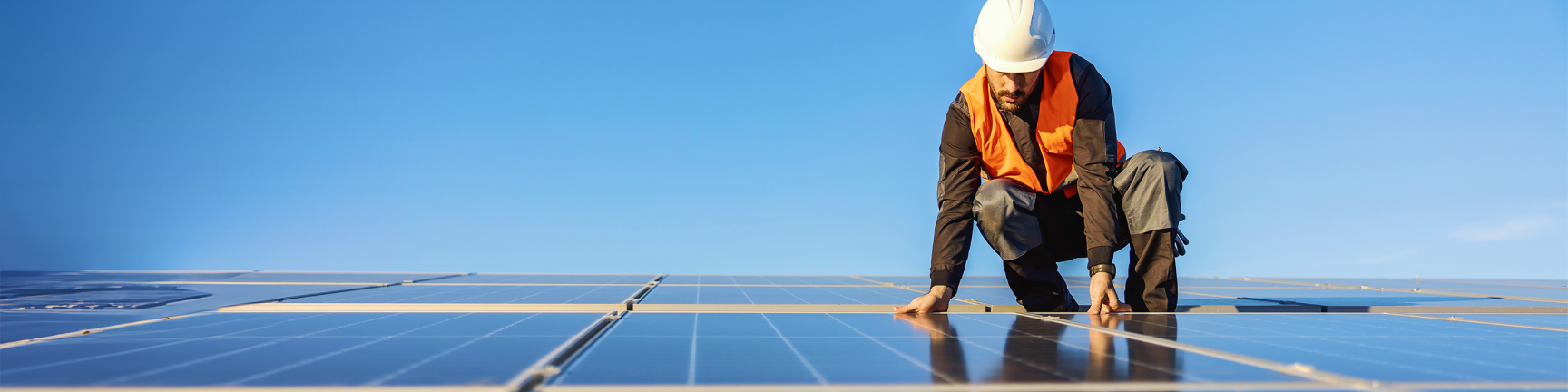 Mann mit Schutzhelm auf Solarmodulen