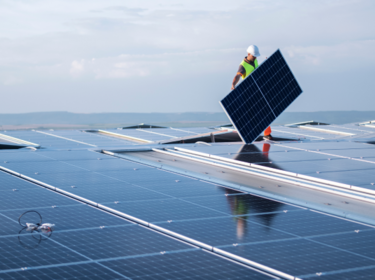 Arbeiter mit Schutzhelm, der Solarmodul auf dem Dach hält